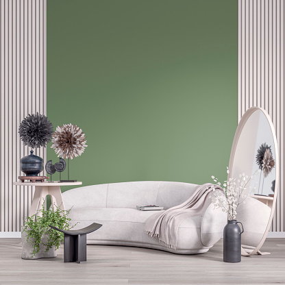 Front view of a cozy, elegant, and modern living room with a round shaped white velvet sofa, tables, an elliptical mirror with decoration (a blanket, a book, sculptures, dried plants, vases, pots, potted plants) in front of a half plaster sage green wall background, half natural white wood panelled wall with copy space. A slight vintage effect was added. 3D rendered image.