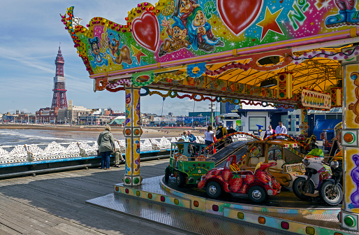 View towards Blackpool tower from the pier in the centre of Blackpool, UK.  A fairground ride can be seen in the foreground and people can be seen on the pier.