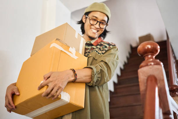 istock Smiling young asian man carrying boxes moving to new house 2148127107