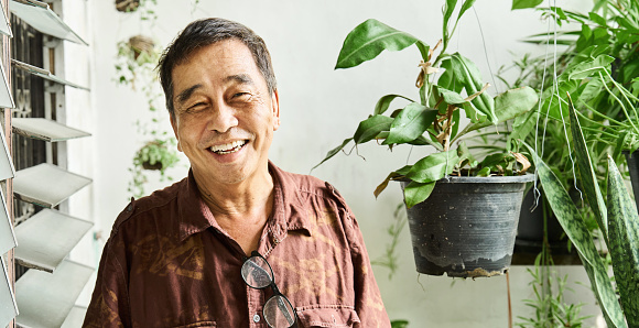 Portrait of a mature man laughing while doing some gardening with potted plants outside on his apartment balcony