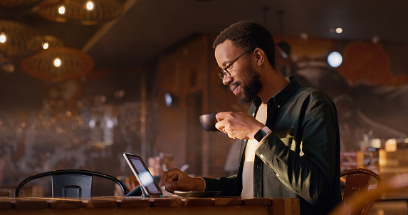 Happy black man, tablet and restaurant with coffee for morning, remote work or research. African male person or freelancer with smile, latte or cappuccino on technology for online networking at cafe