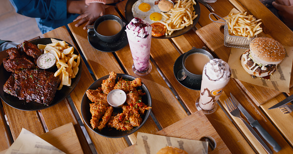 Top view, fast food on table at restaurant for dinner or lunch, people with cuisine and catering. Burger, fries and milkshake drinks with wings for nutrition, eating and hungry for meal for supper