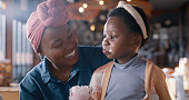 Happy, milkshake and mother with girl in restaurant for lunch, supper and eating meal together. Black family, fine dining and mom with young girl for bonding, relax and fun with drink in cafeteria