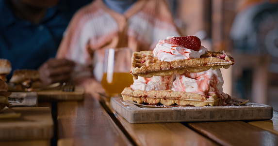 Waffle, dessert and ice cream with wooden board on table for serving at indoor restaurant. Closeup of delicious or sweet treat for snack, meal or tasty food with strawberry, syrup or fruit at cafe