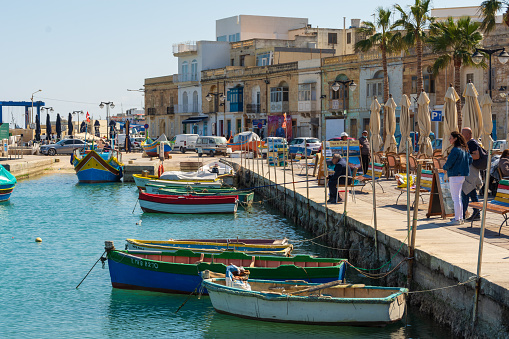 Marsaxlokk, Malta - March 23rd 2022: Rowboats moored in Marsaxlokk Harbour next to the promenade.