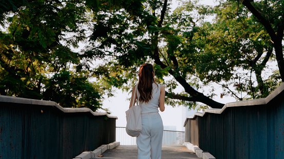 A woman walks across a bridge surrounded by lush greenery, symbolizing tranquility and forward movement