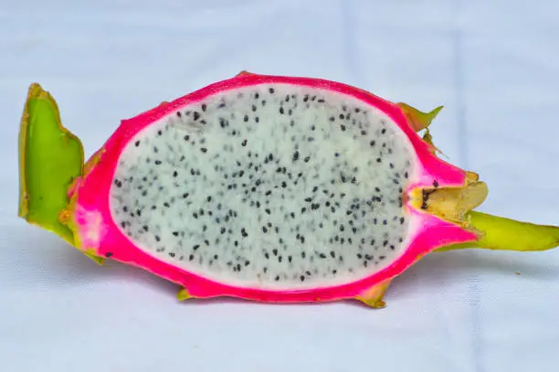 Close-Up Of Texture Of White Flesh And Black Seeds Of Sliced Dragon Fruit Against White Background