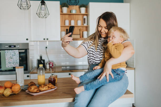 istock Mother and little son sitting on kitchen table and having video call on smart phone during breakfast at home 2148132157