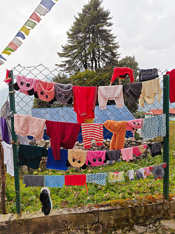 Colorful clothes hanging on a wire fence with prayer flags and trees in the background.