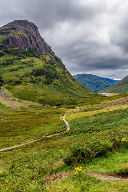 Hiking trail leading into a valley surrounded by steep mountains and a stormy, grey sky