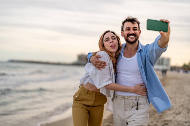 istock Man taking selfie on cellphone with girlfriend showing tongue 2148135695