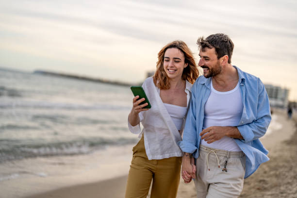 istock Young happy couple reading a text message on smart phone during summer day on the beach. 2148135752