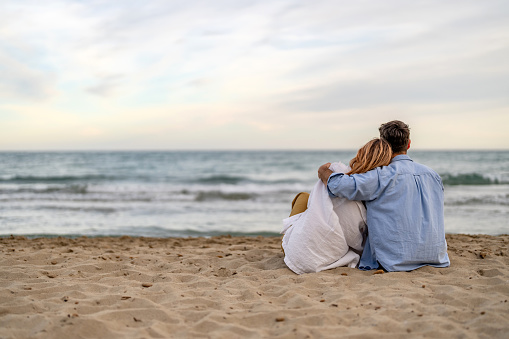 Couple sitting on sandy beach at water's edge