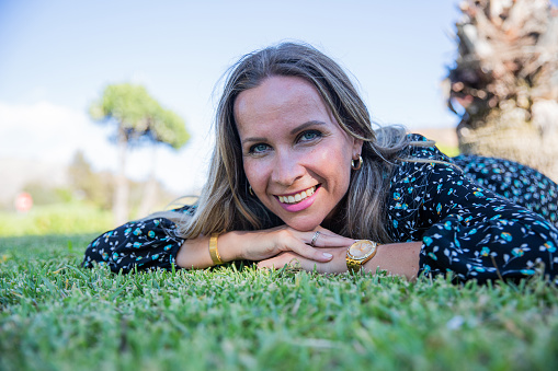 Portrait of a smiling woman laying on the grass with her face on her hands.