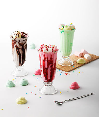 Three decadent milkshakes topped with marshmallows and meringues. Chocolate, strawberry and lime