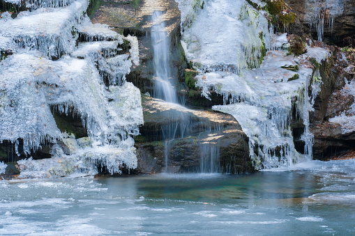 Waterfall cascades down cliff into icy pool in winter