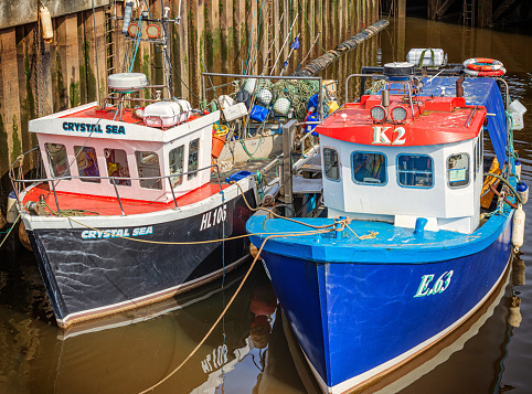 Whitby, UK.  March 31, 2024.  Two small fishing boats in Whitby harbour reflected in the water. The decks are loaded with fishing gear including nets and marker buoys.