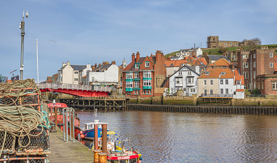 Whitby, UK.  March 31, 2024.  Boats are moored to a quay in harbour.  Behind is a bridge and buildings are on the far side of the harbour. Ropes and lobster pots are on the foreground.