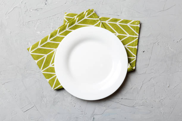 istock Top view on colored background empty round white plate on tablecloth for food. Empty dish on napkin with space for your design 2148140958