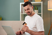 Young man shopping online, holding a credit card and using a laptop computer.