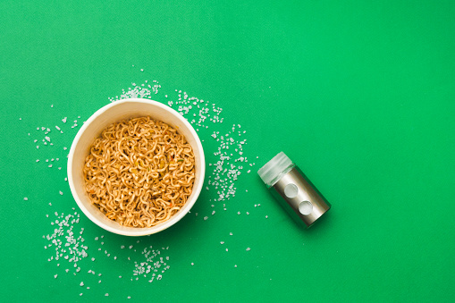 Wok noodles and salt shaker on a green background. Please add salt to your food in moderation. Too much salt in food is harmful to health. Flat lay.