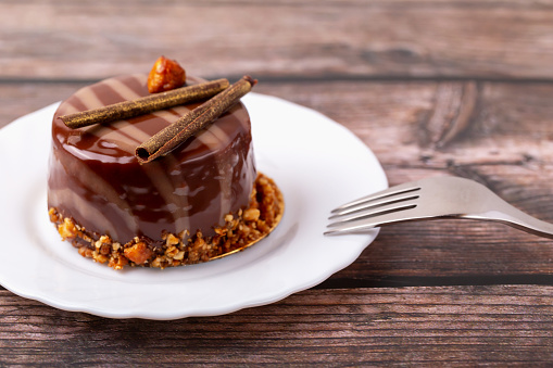 Fresh delicious chocolate cake on plate with fork on wooden background close-up. Caramel glaze and decoration add appeal and desire