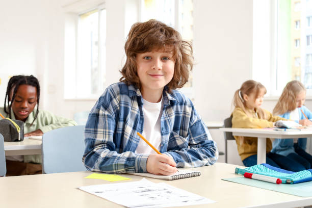 istock Smiling Caucasian schoolboy writing during the lesson, sitting at the desk while studying 2148145268