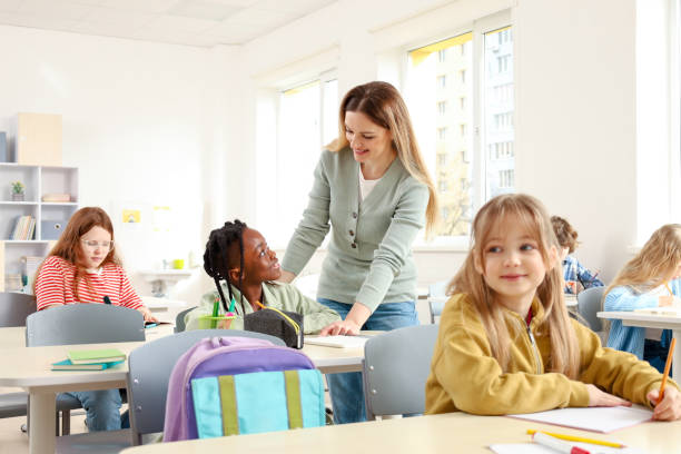 istock Teacher helping pupils studying at desks in classroom. Education, learning and people concept 2148145274