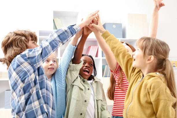 istock Team of young kids joining their hands while standing in the classroom at school 2148145334