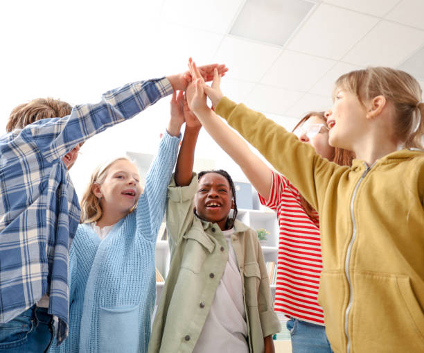 istock Smiling pupils standing and joining their hands up in the classroom at school 2148145344