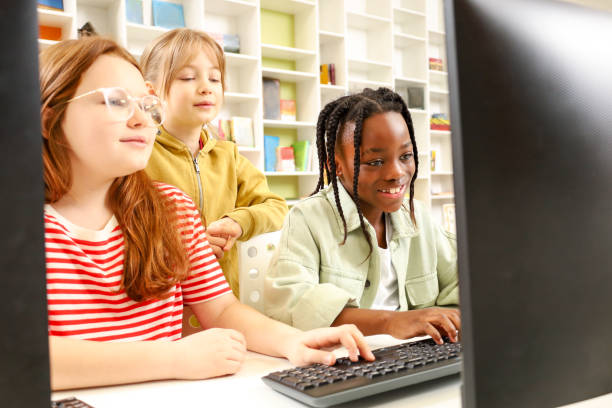 istock Happy kids sitting at the desk in classroom while typing on the computer 2148145384