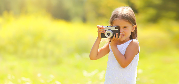 Happy child with film camera taking picture outdoors on sunny summer day