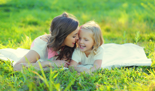 Portrait of happy cheerful smiling mother with little girl child daughter on the grass in sunny summer park