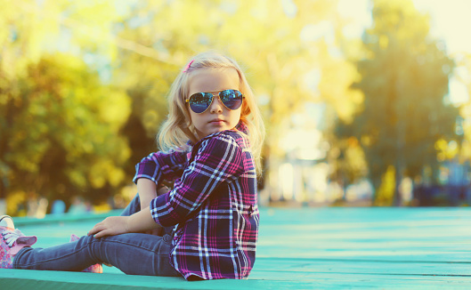 Stylish little girl child posing in sunglasses in sunny summer park
