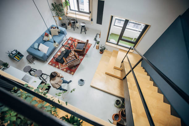 Woman using smart phone to control robotic vacuum cleaner in beautiful modern loft apartment.