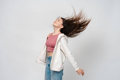 Portrait of beautiful hispanic brunette girl with closed eyes, hair flying to the sides isolated on gray background. Attractive teenage girl wearing casual outfit is happy, copy space