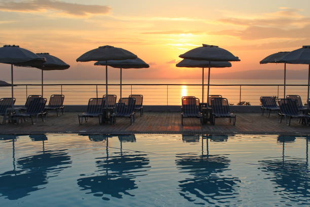 A tranquil image of a beach lined with vibrant yellow parasols, viewed from an infinity pool that seamlessly blends into the shoreline. The soft hues of an early sunset paint the sky in warm tones, reflecting beautifully on the water. This idyllic scene captures the essence of late afternoon relaxation on a perfect vacation, evoking feelings of peace and luxury.