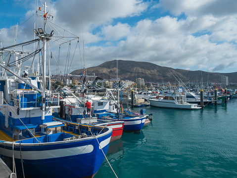 Los Cristianos, Tenerife, Canary Islands, Spain, december 26, 2021: Port of Los Cristianos, small harbour with fishermans boat and sailing ships and city building at background. Sunny day