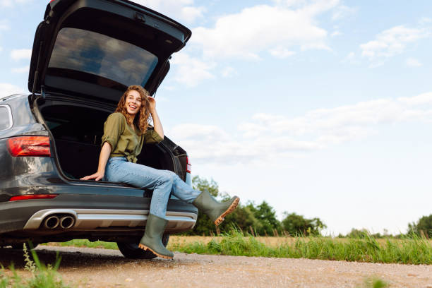 istock Young woman enjoying fresh air sitting in open trunk. 2148149696
