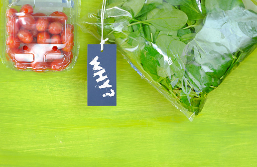 plastic wrapped food, spinach and tomatoes in plastic bags,sign with caption