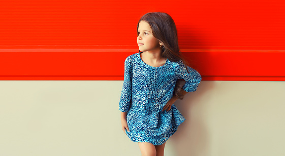 Portrait of beautiful little girl child looking away in blue dress on red background