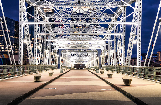 Lights illuminating the metal framework of the Shelby Street Bridge at dusk, leading to downtown Nashville.