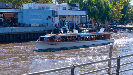 Tigre, Buenos Aires, Argentina. 03-29-2024. Old typical wooden small transport ship sailing in a narrow river in Tigre with tourist inside. Taken on a warm autumn mornng