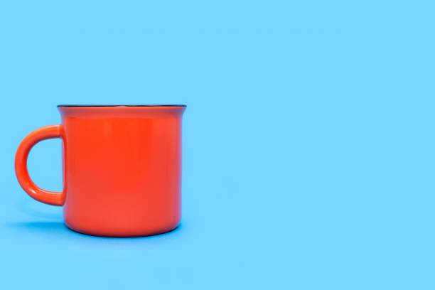 Orange mug on a blue background with free space for text. Orange cup with a drink on a blue background. Coffee house concept. Orange mug with the possibility of applying advertising or logo