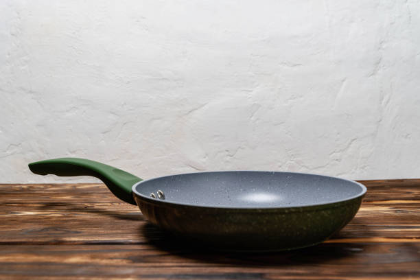 A frying pan is placed on a wooden table, ready for cooking or serving food.