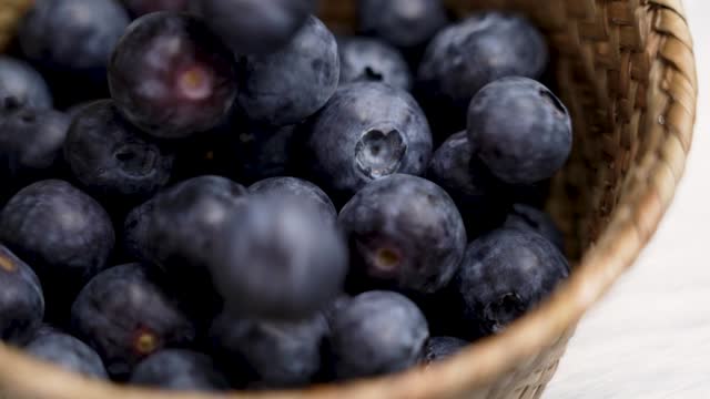 Fresh blueberries falling into a rustic wicker bowl in slow motion. Delicious organic blue bilberry close up. Rural style view