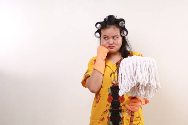 Side view of aged 40-44 years old who is beautiful with long hair caucasian young women caretaker standing in front of white background wearing apron who is smiling who is cleaning and holding broom