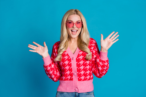 Photo of eccentric impressed woman with wavy hairdo dressed pink jumper raising palms announcing sale isolated on blue color background.