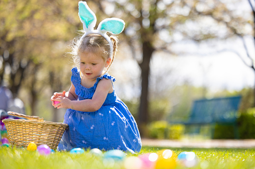 A little girl on an easter egg hunt outside at the park.