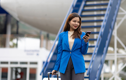 Businesswoman at the airport carries a suitcase, prepares to board the plane and depart. Asian female tourist at airport using smartphone to contact someone.